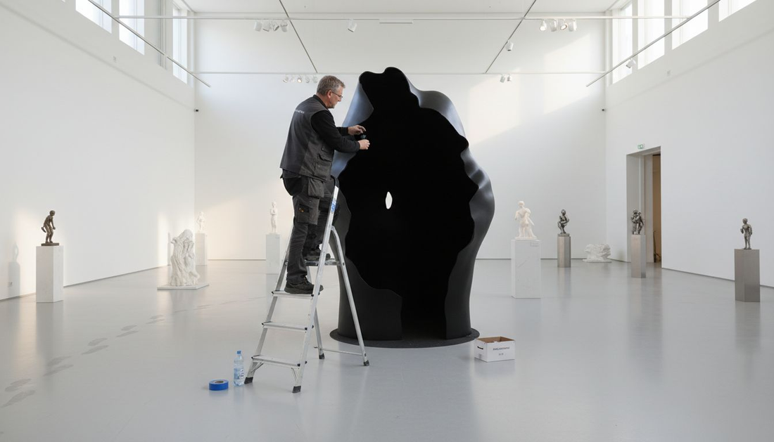 Gallerian työntekijä viimeistelee ultra­mustaa taideteosta näyttelytilassa.